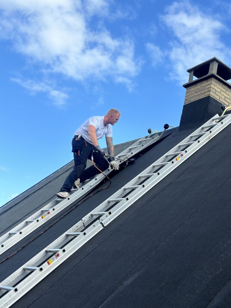 Håndværker arbejder på tag under blå himmel